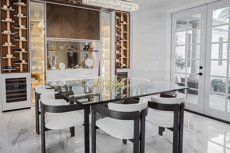 Dining room with a glass table, wine display, and illuminated glass-front cabinetry.